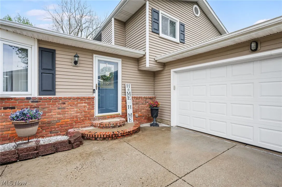 Exterior of a tan house with a brick foundation, blue door, white garage door, and "HOME" sign.