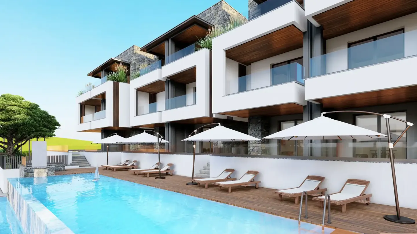 Modern white condos overlook a blue pool with lounge chairs and umbrellas on a wooden deck.