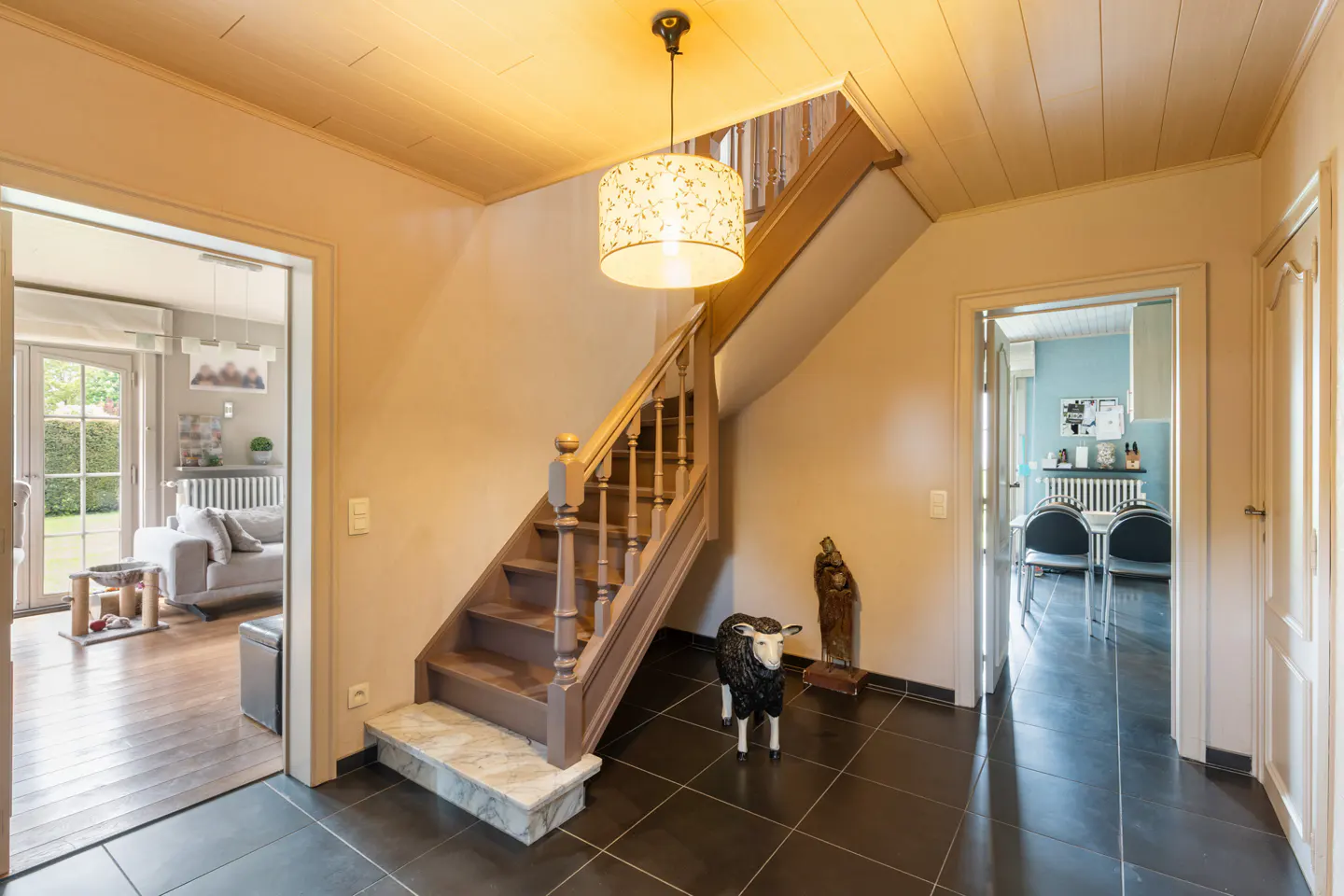 Interior view of a home's foyer with a staircase, black tile floor, and two doorways leading to other rooms. A decorative sheep statue stands near the stairs.