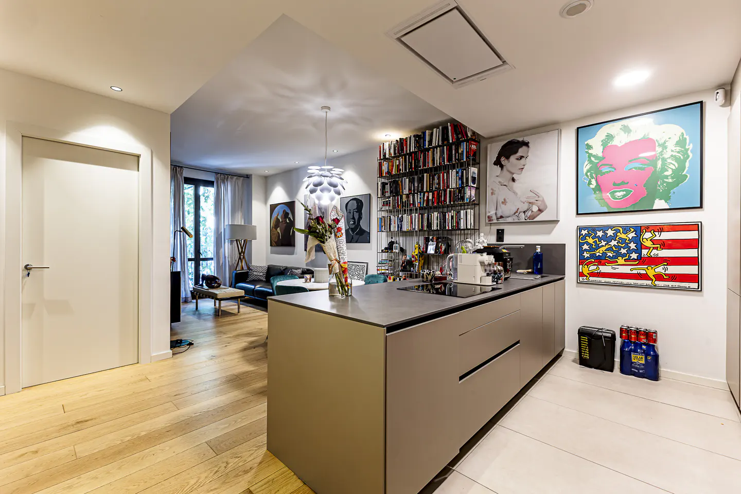 Open-concept kitchen and living room with modern decor. Gray island, hardwood floors, and pop art on the walls.