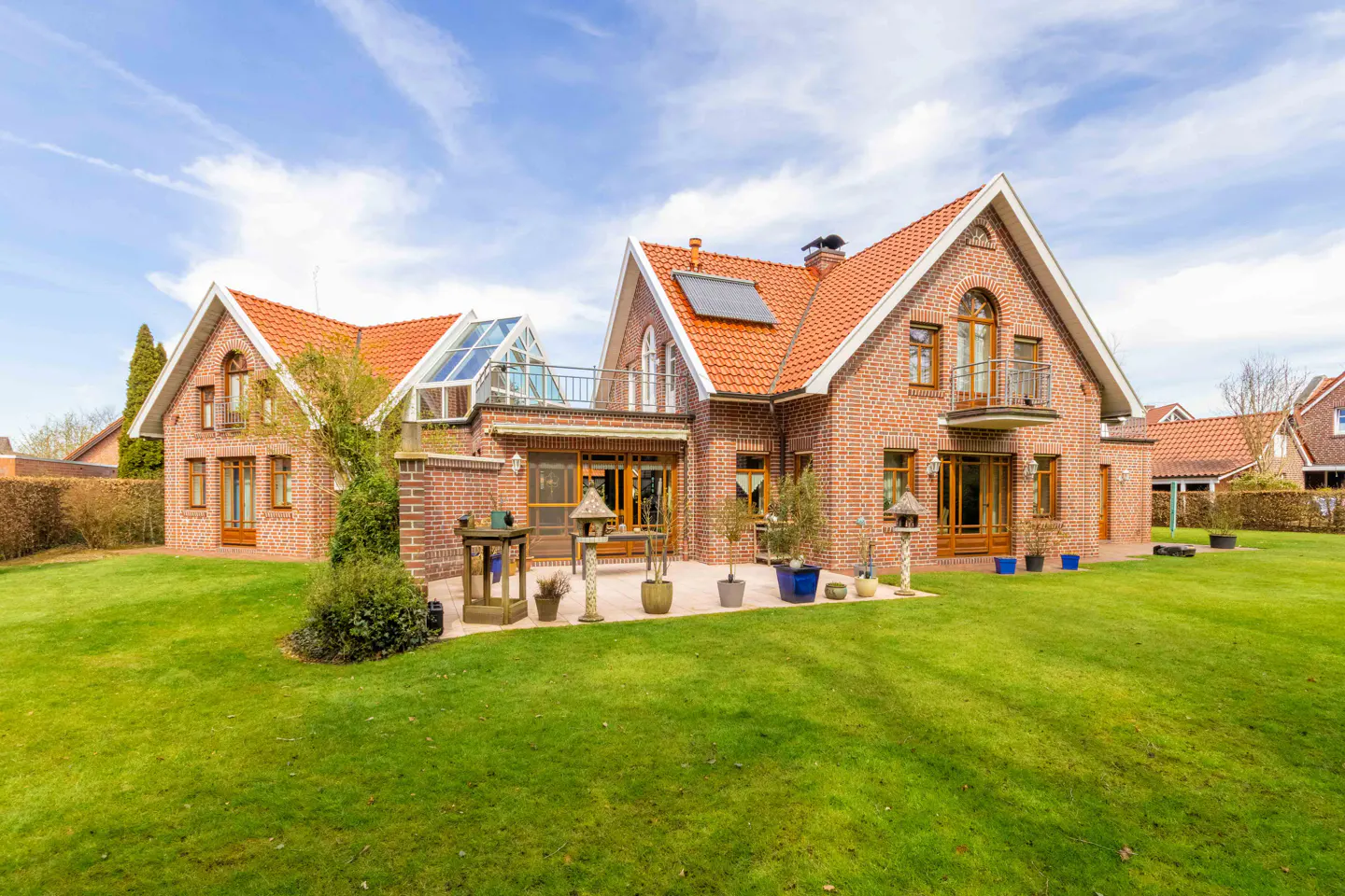 Brick house with a red tile roof, glass conservatory, and green lawn under a blue sky.
