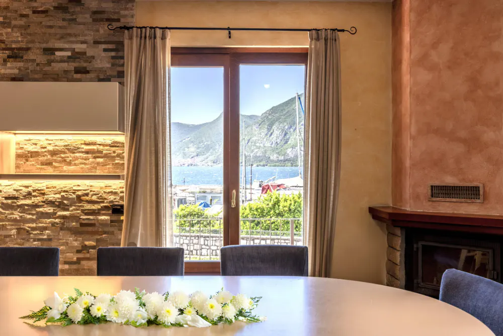 Interior view of a dining room with a round table, white flower centerpiece, and a window view of mountains and water.