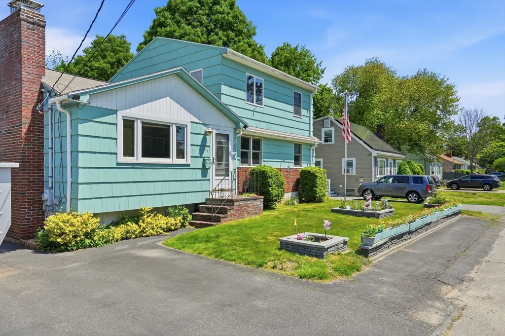 Two-story, light blue house with a brick chimney, green lawn, and black asphalt driveway.