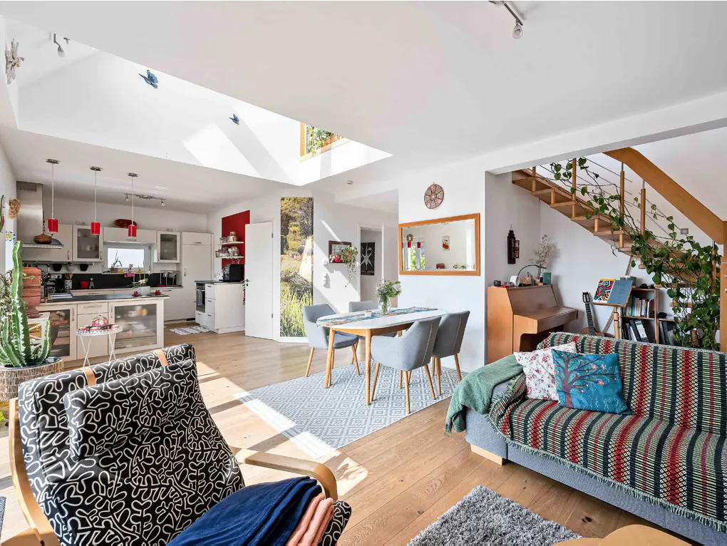 Bright, open-concept living space with wood floors, a kitchen, dining area, and stairs. A patterned chair and sofa add character.