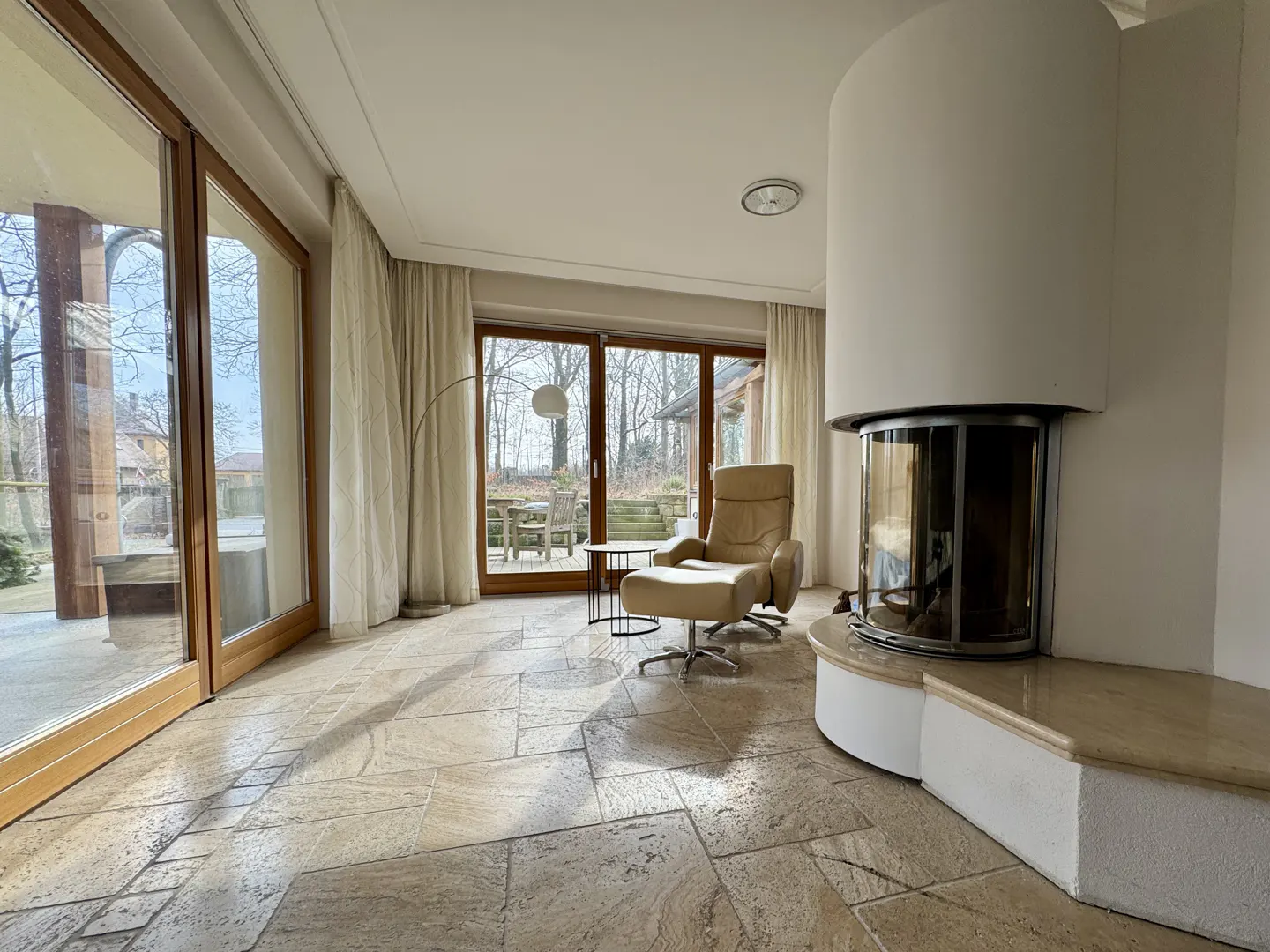 Bright living room with stone floors, a tan leather recliner, and a modern white fireplace. Sliding glass doors lead to an outdoor patio.