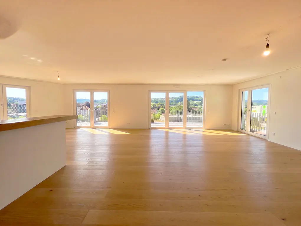 Spacious, empty room with light wood floors, white walls, and large glass doors opening to a scenic outdoor view.