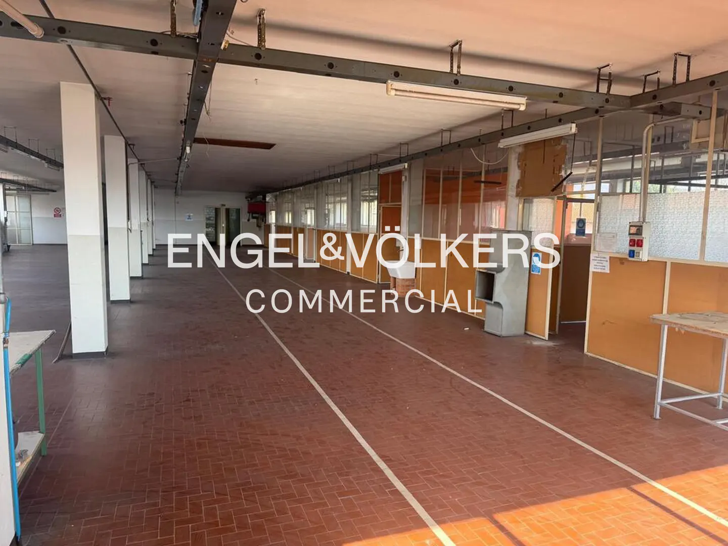 An Engel & Völkers commercial real estate photo shows a large, empty warehouse with red brick floors and white walls.