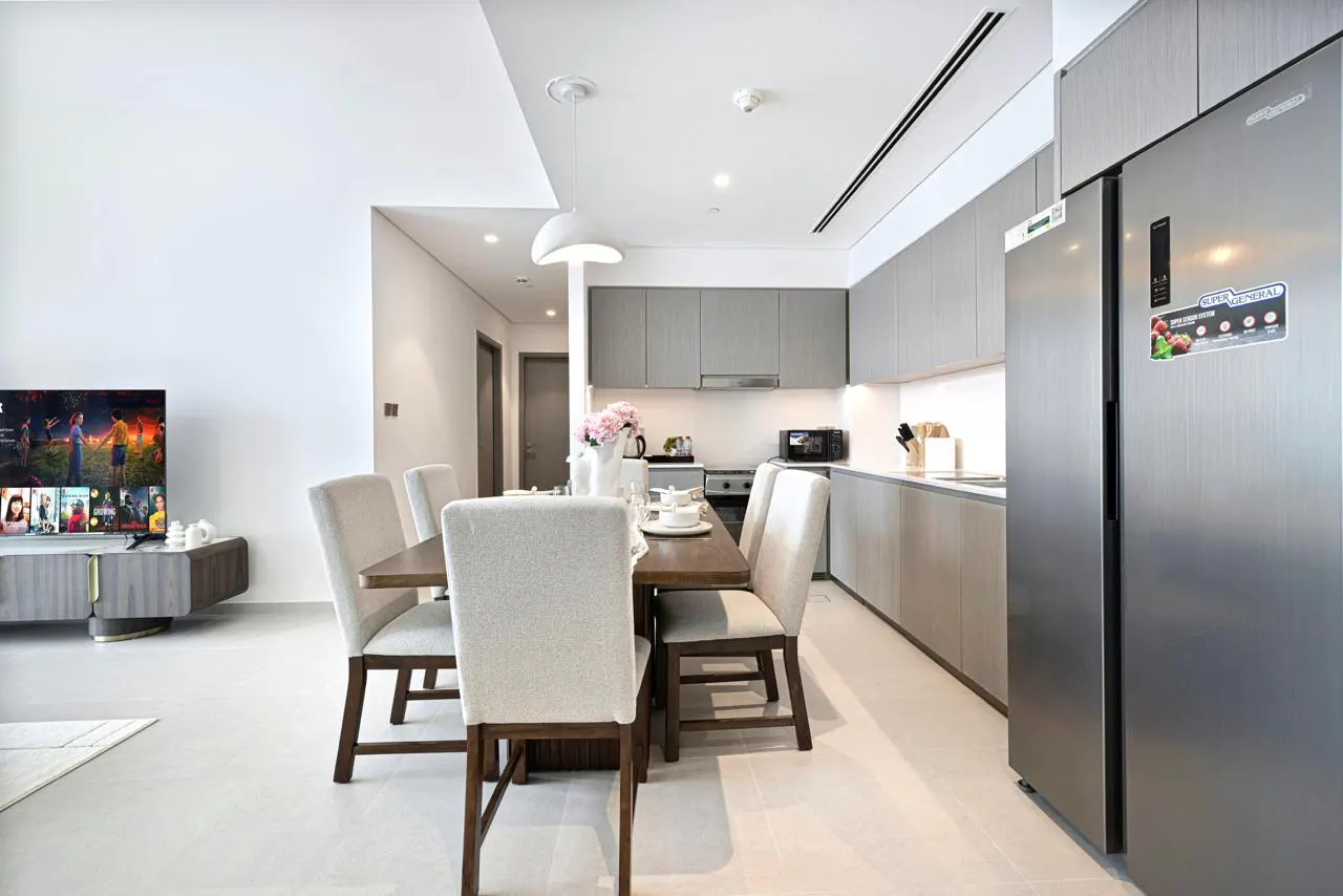 Open-concept apartment with a dining table set for six, a gray kitchen, and a TV showing a movie.