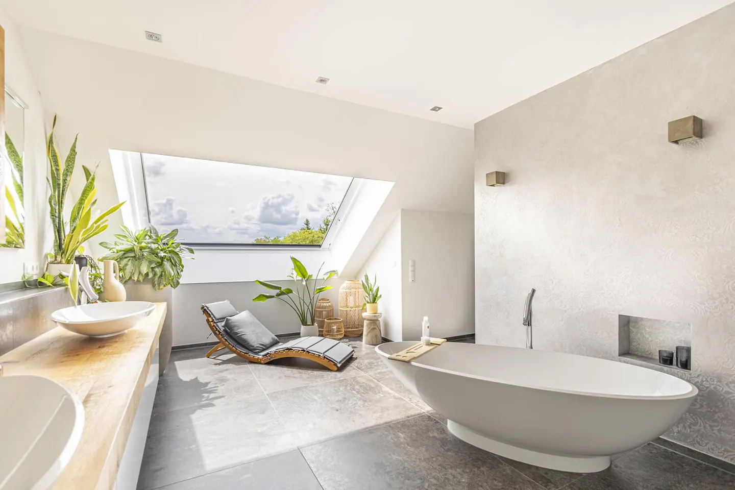 Bright bathroom with a white oval tub, wooden chaise lounge, and a skylight view of the sky.
