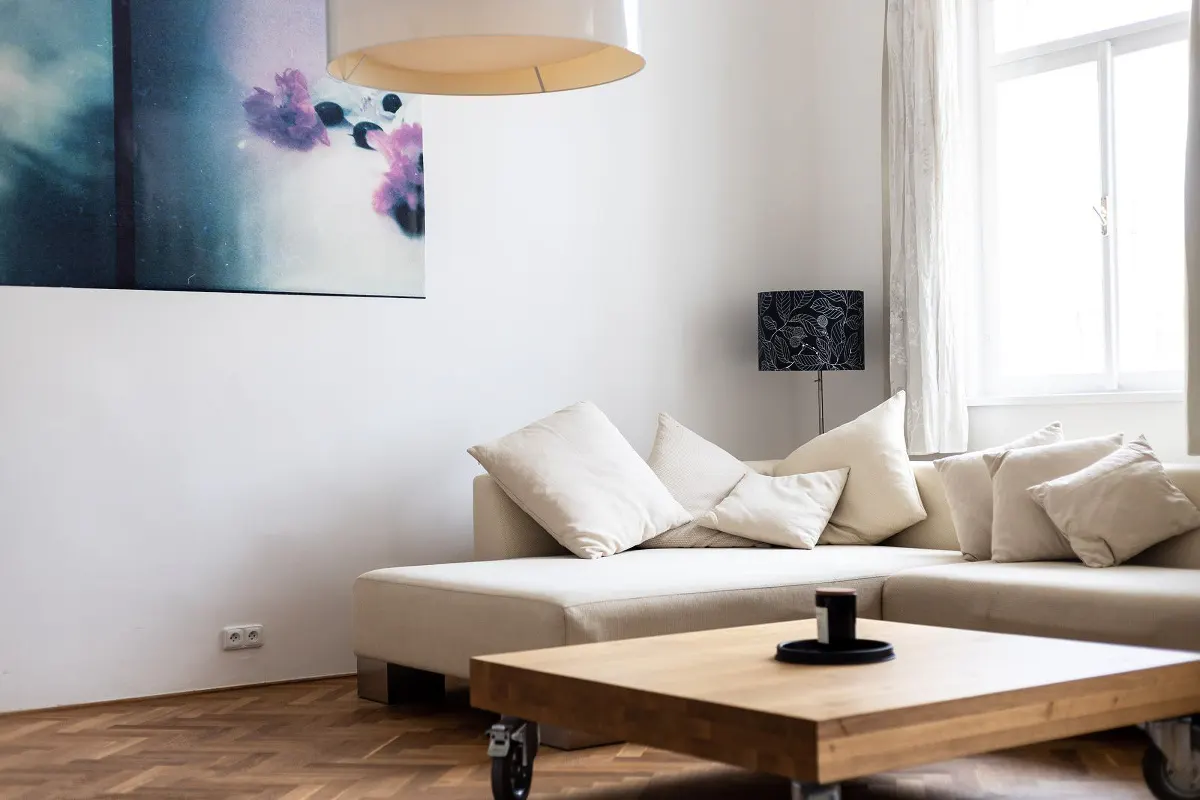 Bright living room with a beige sectional sofa, a wooden coffee table on wheels, and a floral painting on the wall.