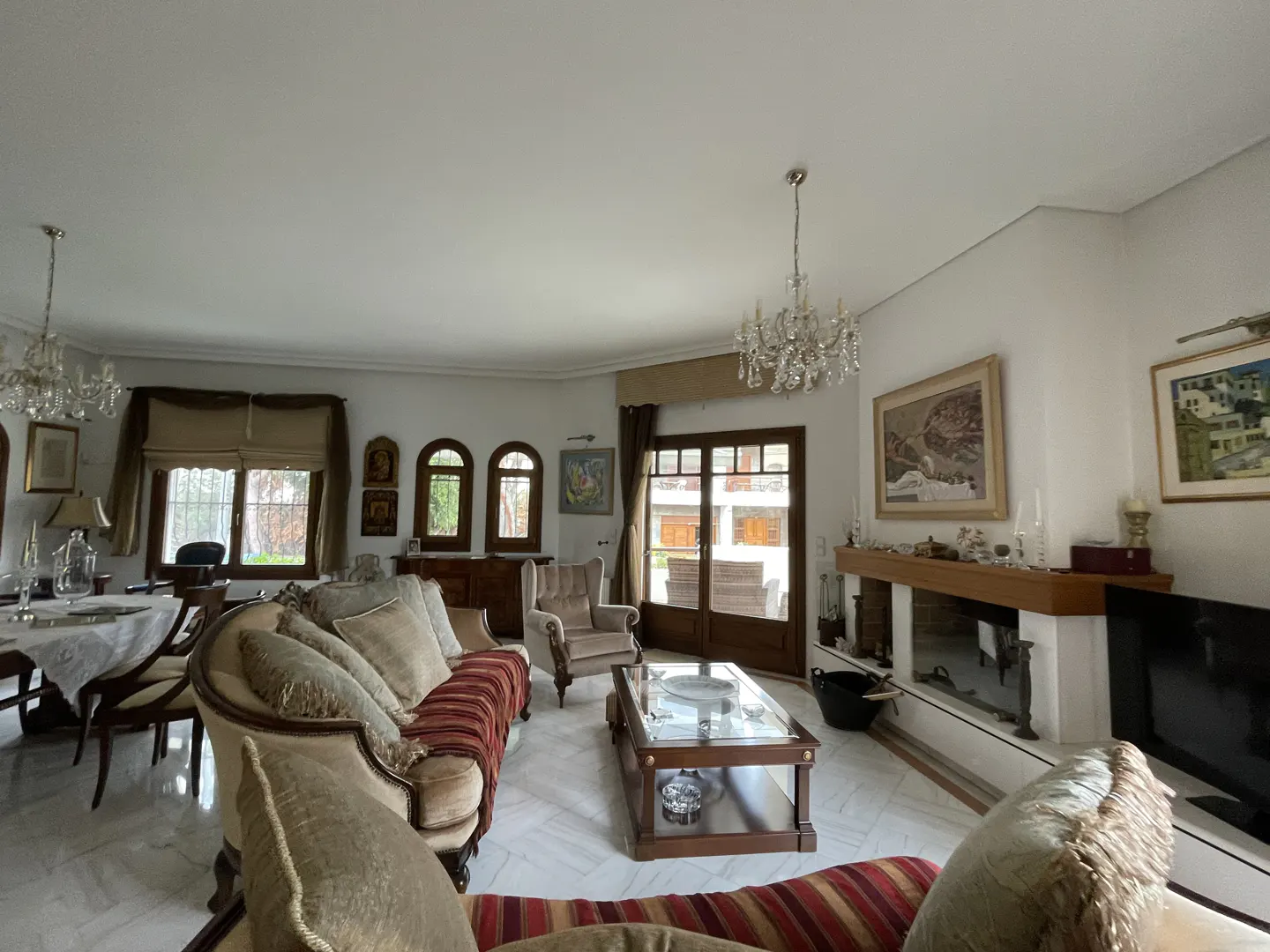 Spacious living room with a striped sofa, glass coffee table, fireplace, and dining area on white marble floors.