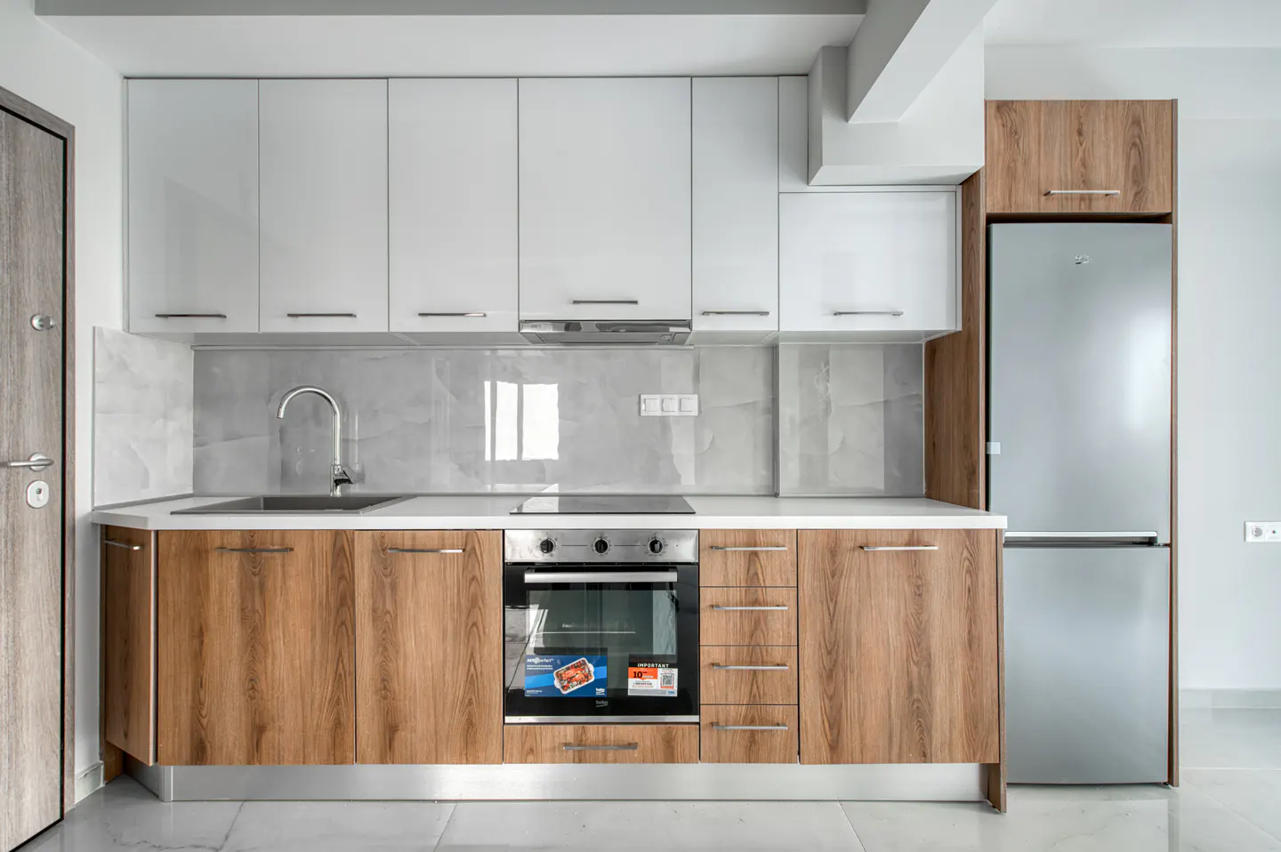 Modern kitchen with white upper cabinets, wood-grain lower cabinets, stainless steel appliances, and marble backsplash.