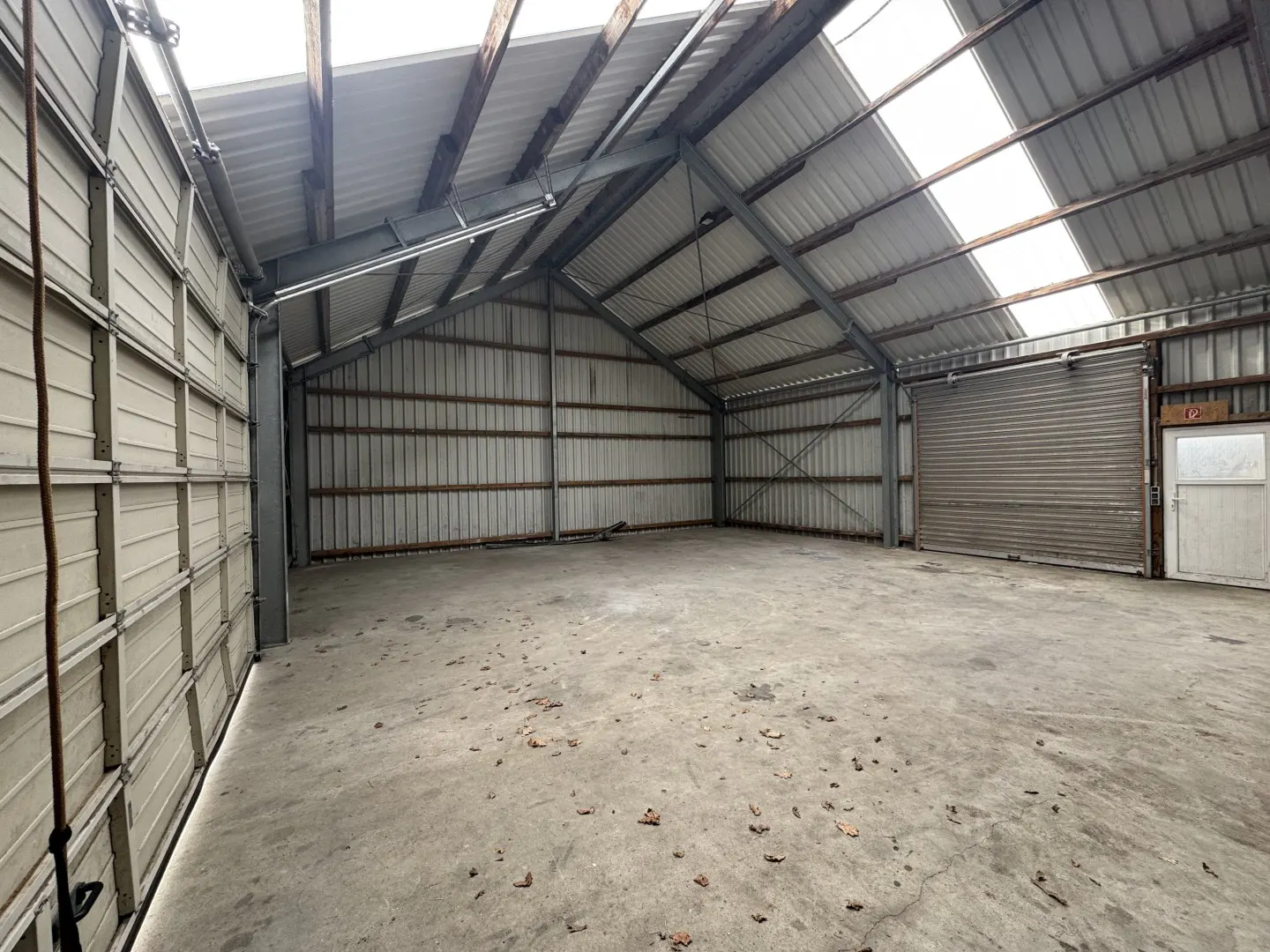 Interior of a large, empty metal warehouse with a concrete floor and a partially open garage door.