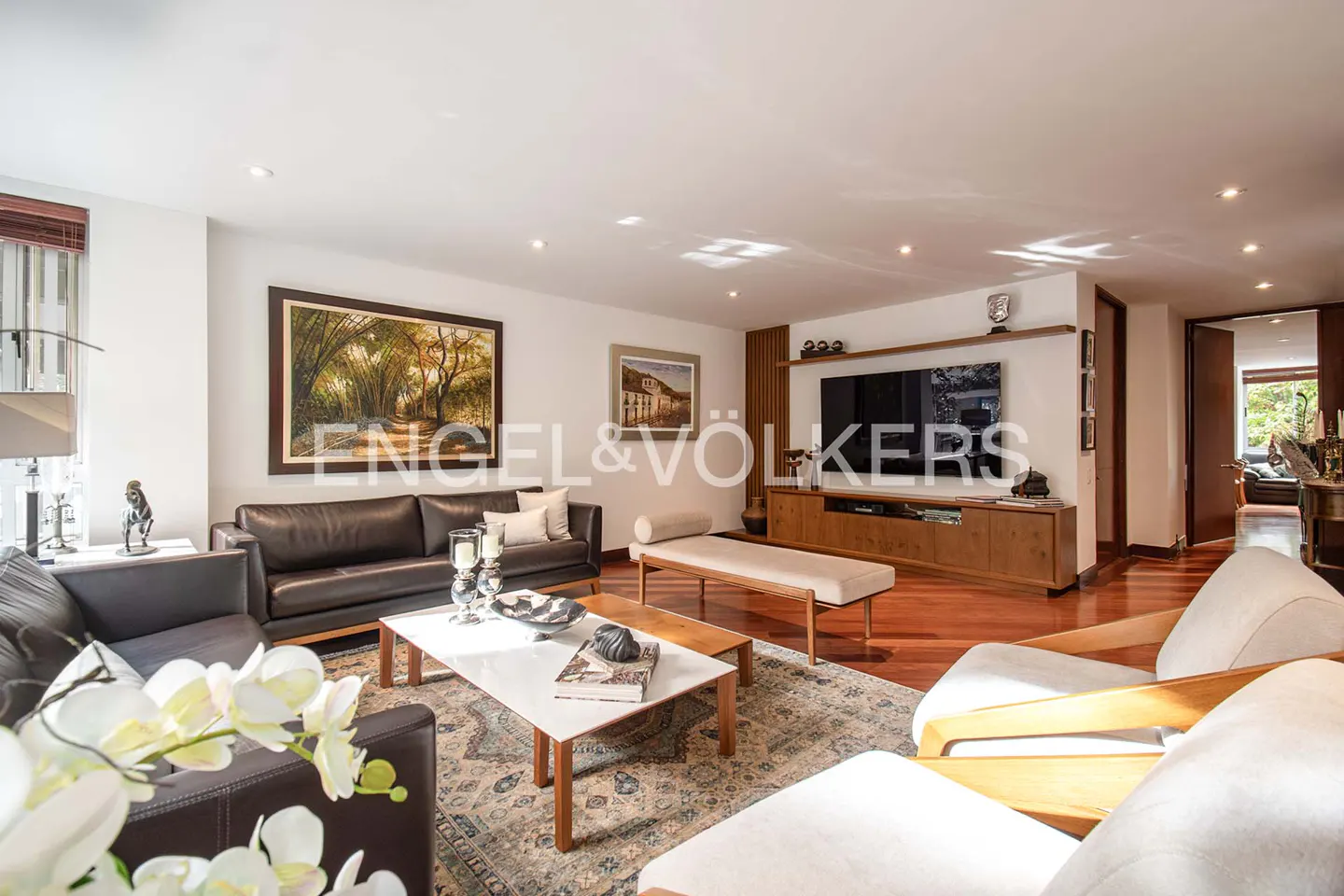 Living room with brown leather sofas, white chairs, a white coffee table, and a large TV on a wooden stand.