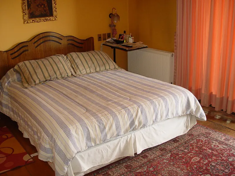 Bedroom with a striped bedspread, wooden headboard, and a red patterned rug. Yellow walls and peach curtains add warmth.