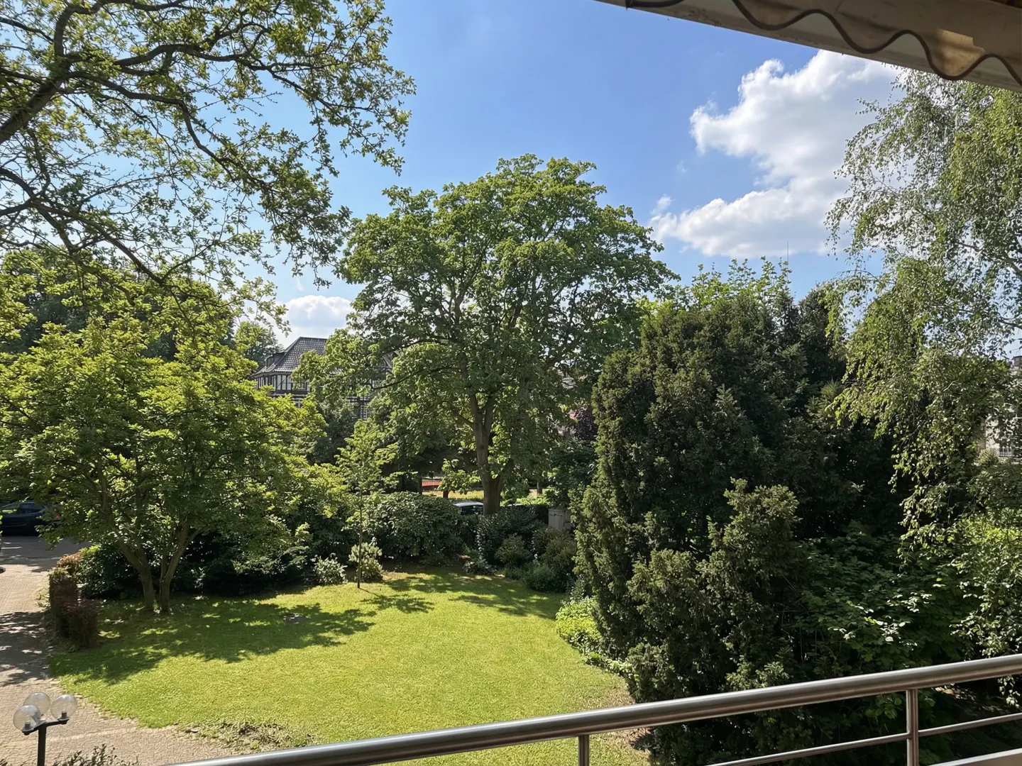 View from a balcony overlooking a green lawn and trees under a blue sky with white clouds.
