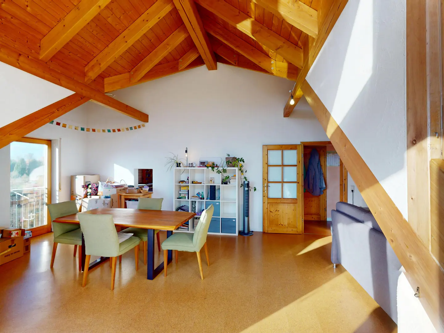 Bright, open living space with wood beams, dining table, and white shelving. Natural light floods the room.