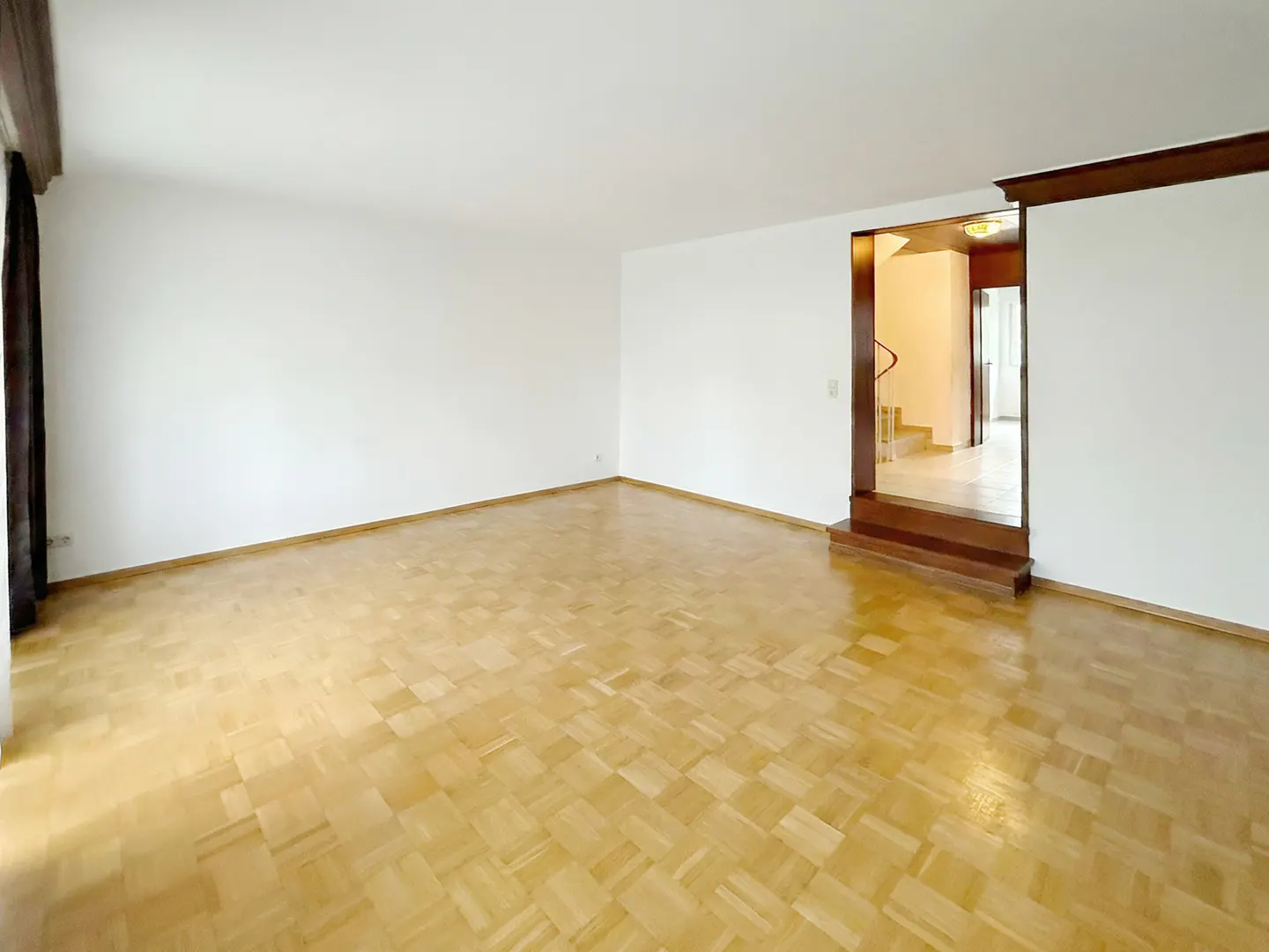 Empty room with parquet floor, white walls, and a dark wood-framed doorway leading to a staircase.
