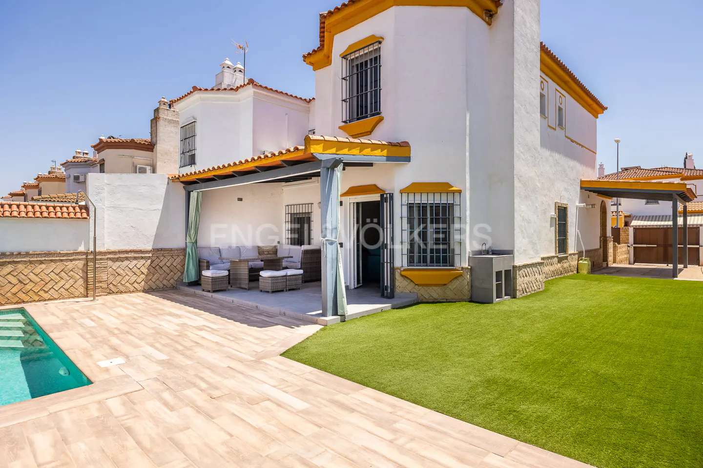 Exterior view of a two-story white house with a pool, patio, and green lawn on a sunny day.