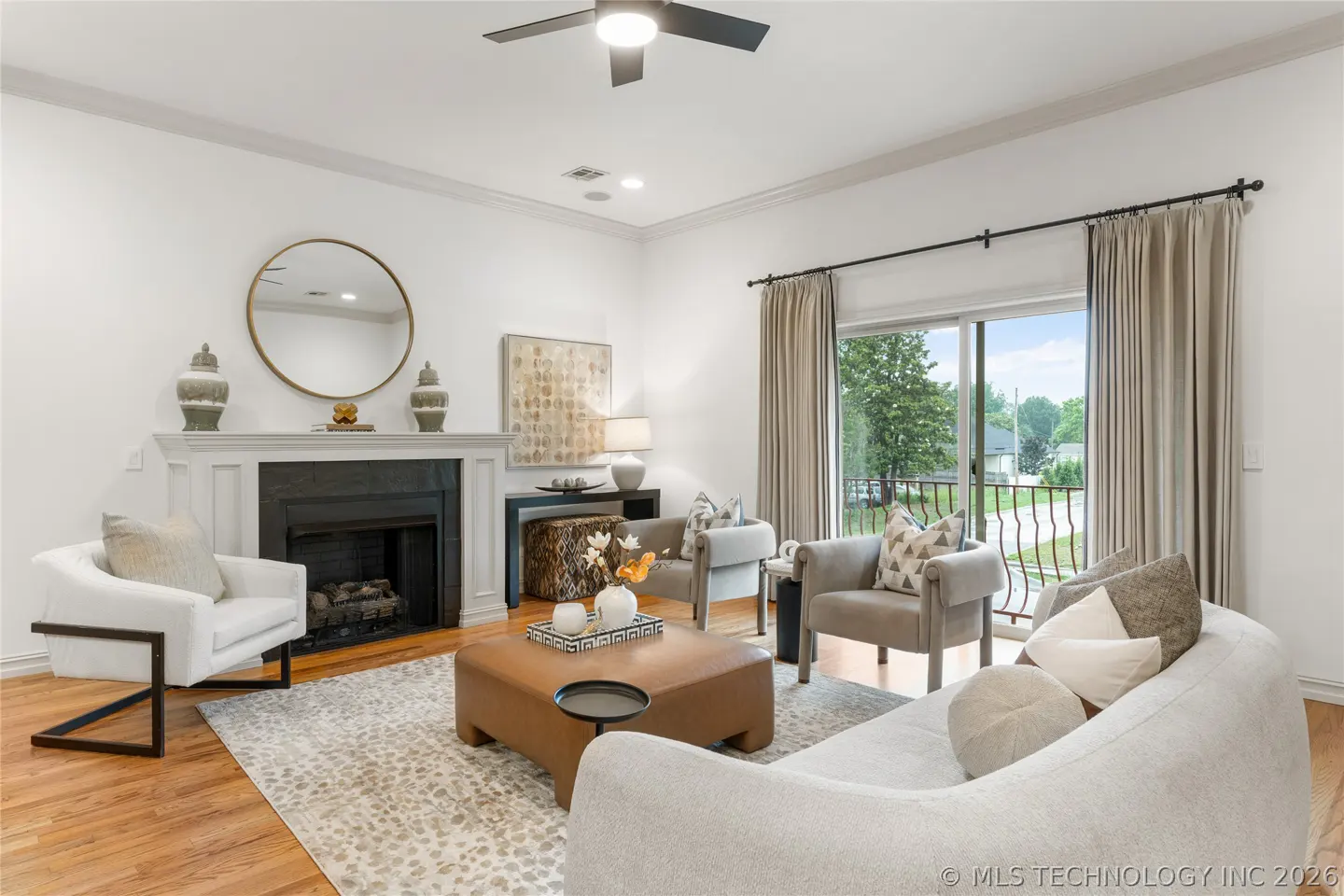 Bright living room with white walls, fireplace, and neutral furniture. A ceiling fan is visible. Sliding glass doors lead to a balcony.