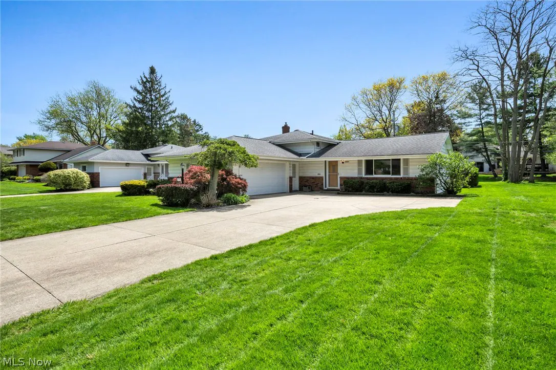 A ranch-style house with a gray roof, white siding, and a two-car garage sits on a green lawn under a blue sky.