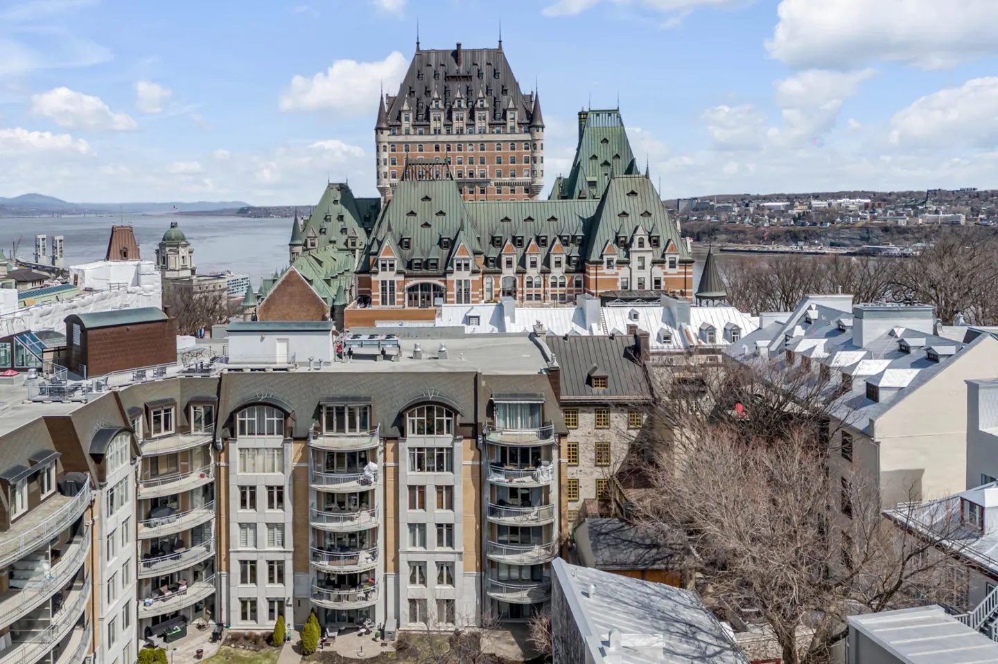 View of a condo building with balconies, with the Château Frontenac in the background on a sunny day.