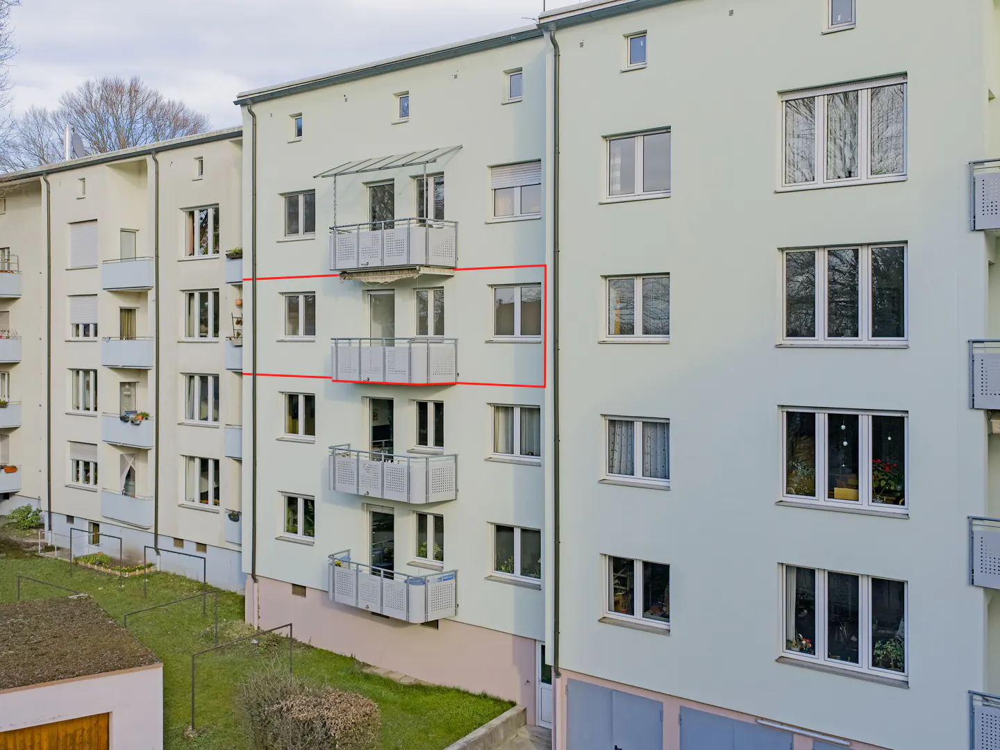 Exterior of a light green apartment building with white balconies and windows, framed in red.