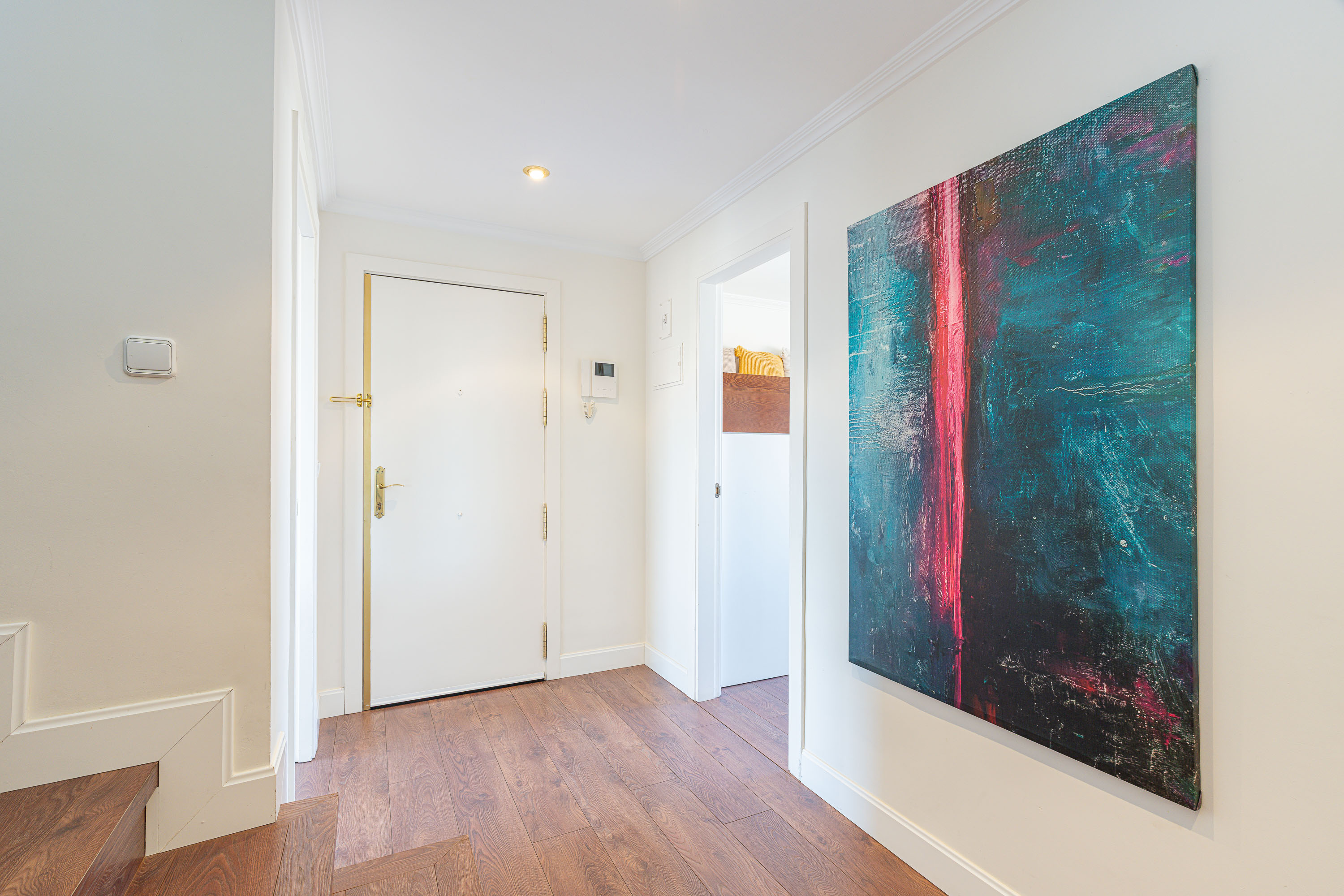 Bright hallway with wood floors, a white door, and a large abstract painting featuring blue and pink tones on the wall. [AI-generated text]