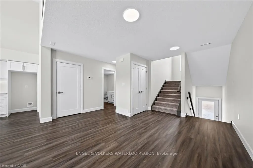 Bright, open-concept home interior with dark wood floors, white walls, and a carpeted staircase. White doors and trim add to the clean aesthetic.