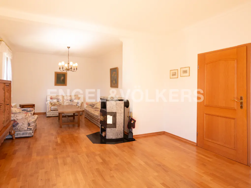 Living room with wood floors, floral sofas, wood-burning stove, chandelier, and a wooden door.