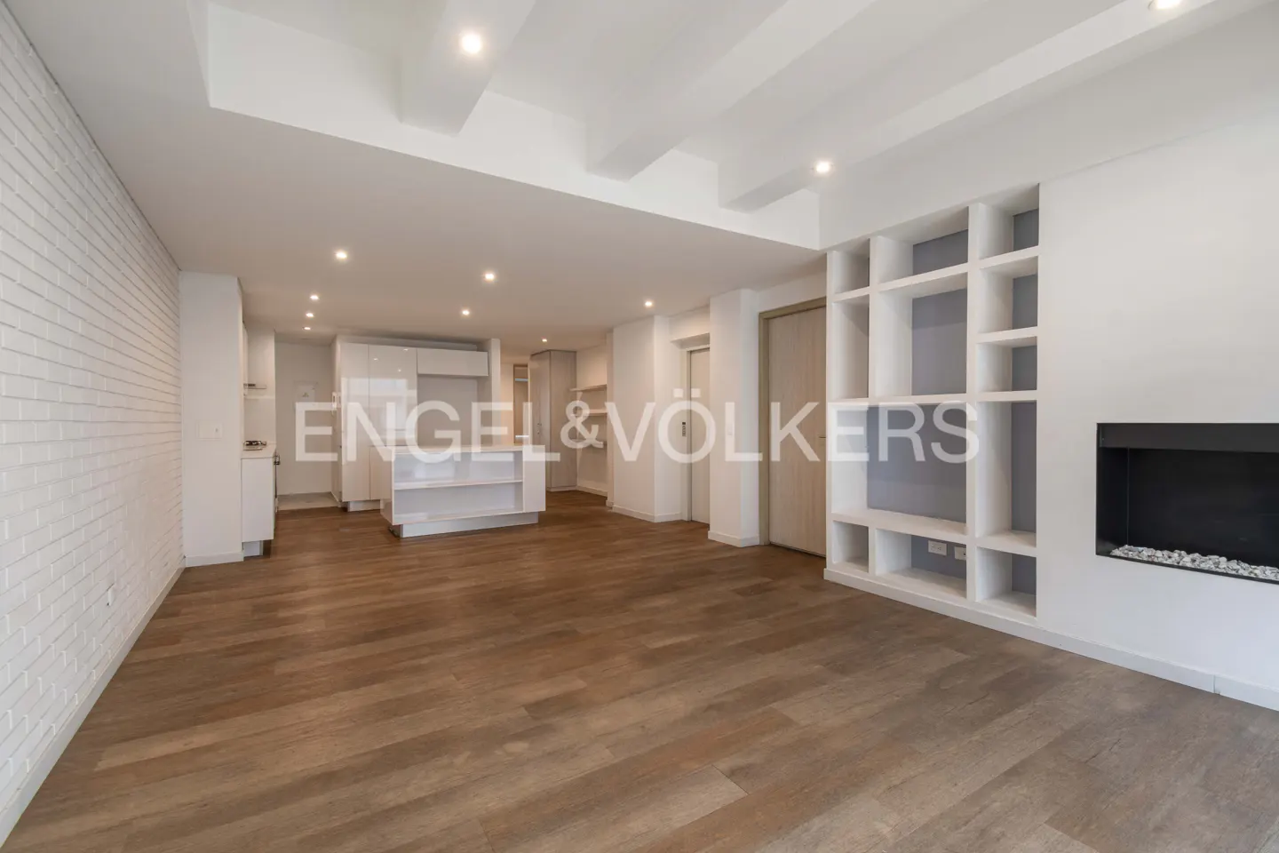 A bright, open-concept living space with wood floors, white brick wall, built-in shelves, and a modern fireplace.