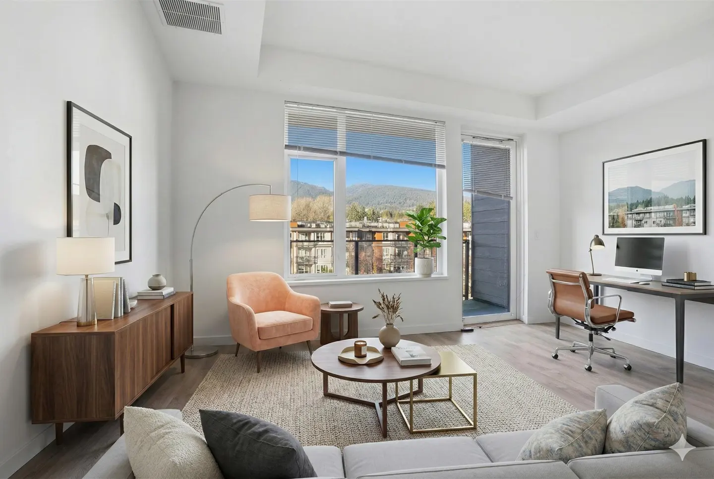 Bright, modern living room with white walls, wood floors, and large windows with mountain views. Features a desk, peach chair, and gray sofa.