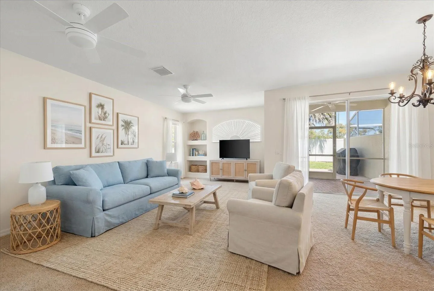 Bright living room with a blue sofa, white armchairs, and a light wood coffee table on a jute rug. Beach-themed art hangs above the sofa.