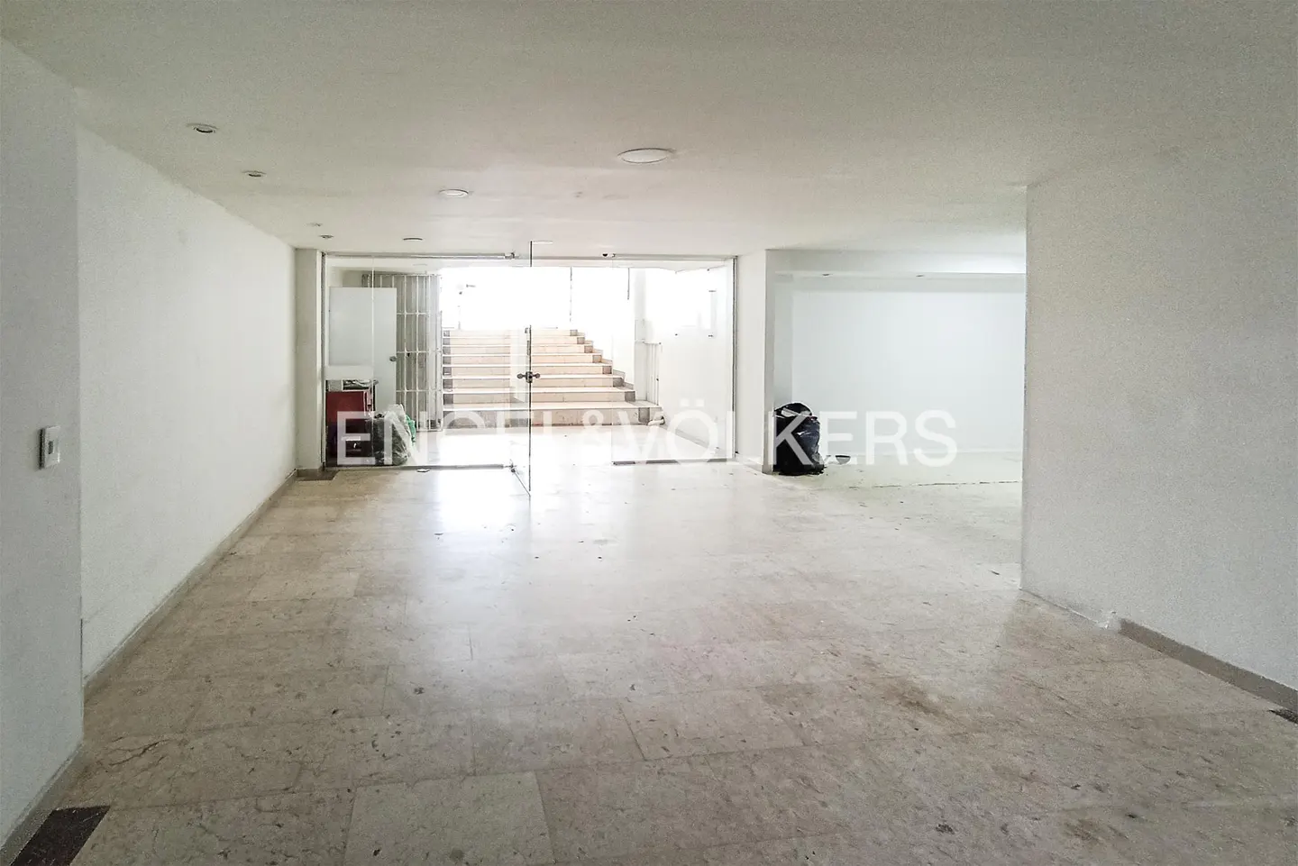 Empty white room with marble floors, glass doors leading to stairs, and Engel & Völkers logo.
