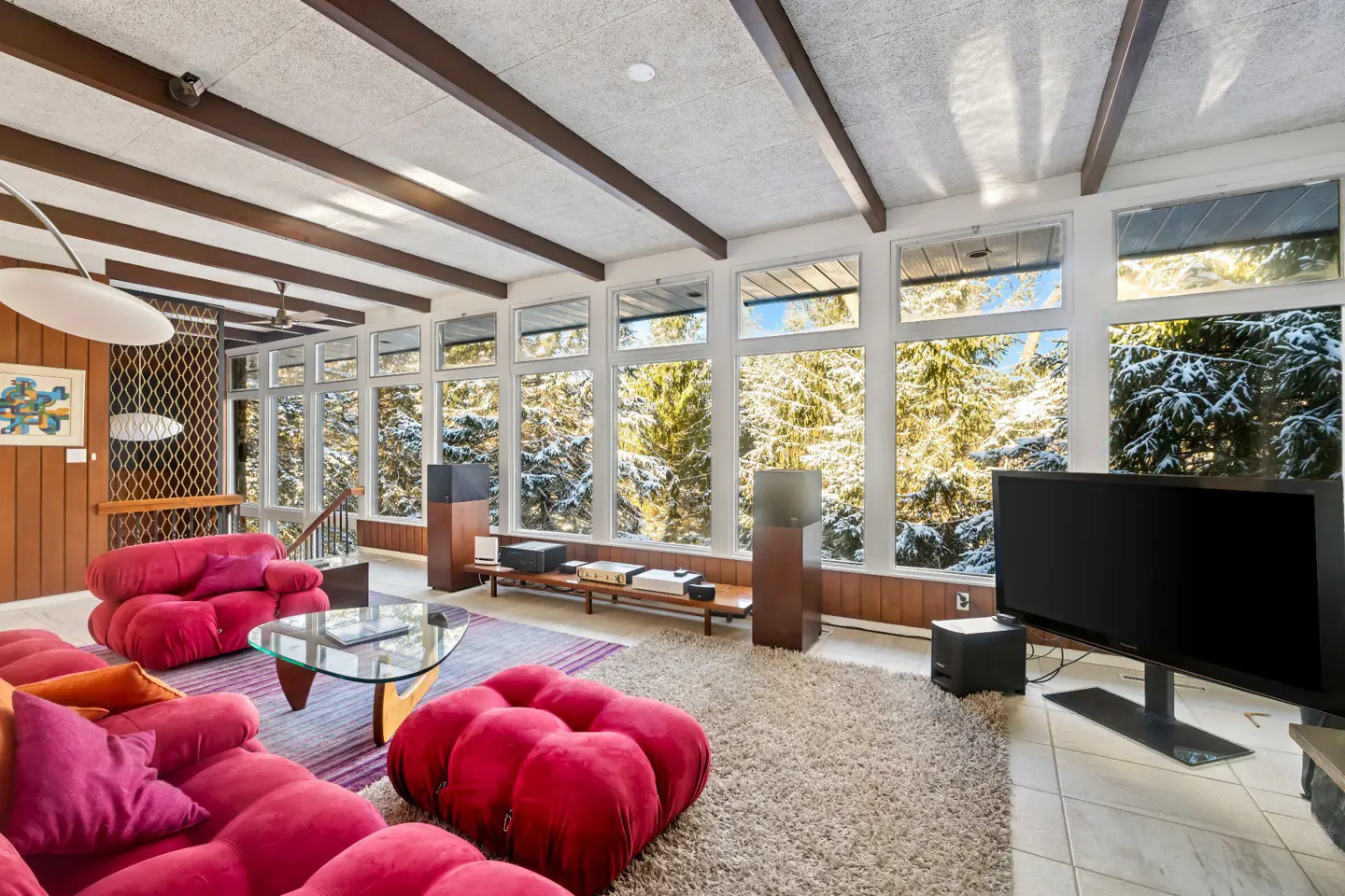 A living room with red sofas, a glass table, and a large window showing snow-covered trees.