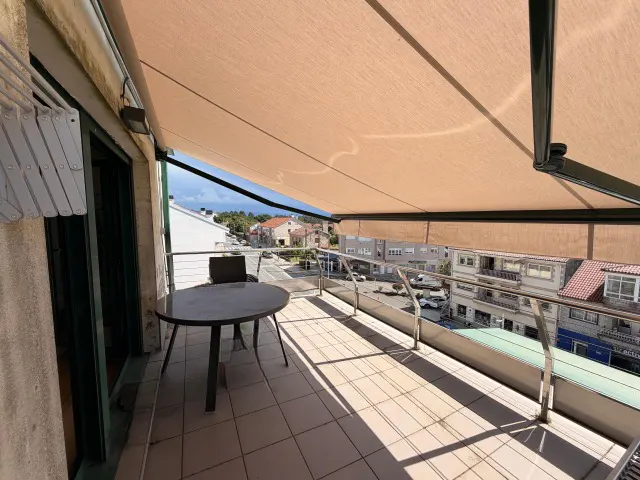 Balcony view with a round table, chair, and awning overlooking a street with buildings and cars.
