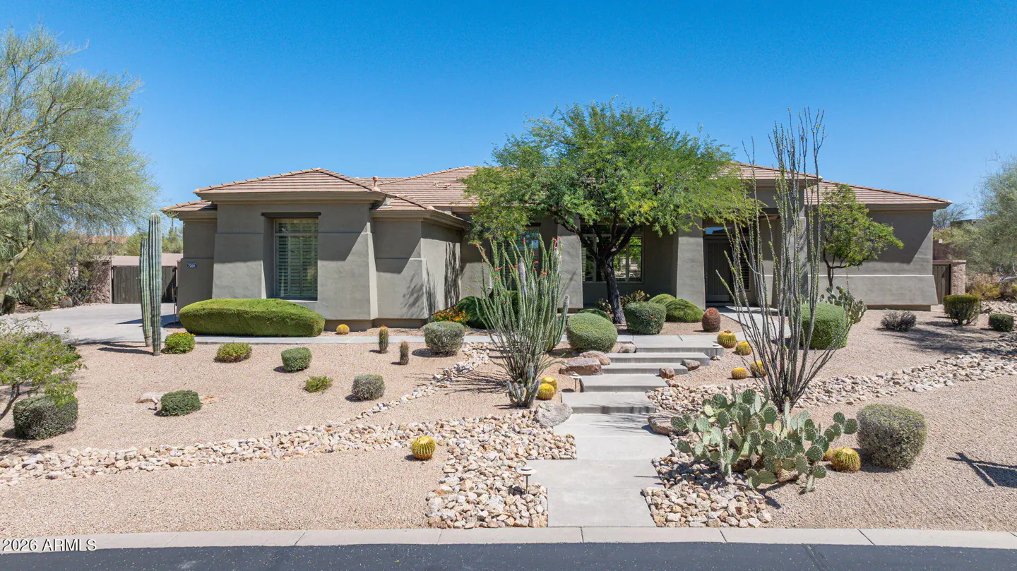 Tan single-story house with a brown roof and desert landscaping under a clear blue sky.