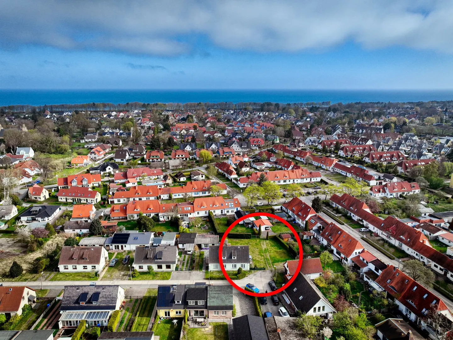 Aerial view of a neighborhood with red-roofed houses near the ocean, with a red circle highlighting a property.