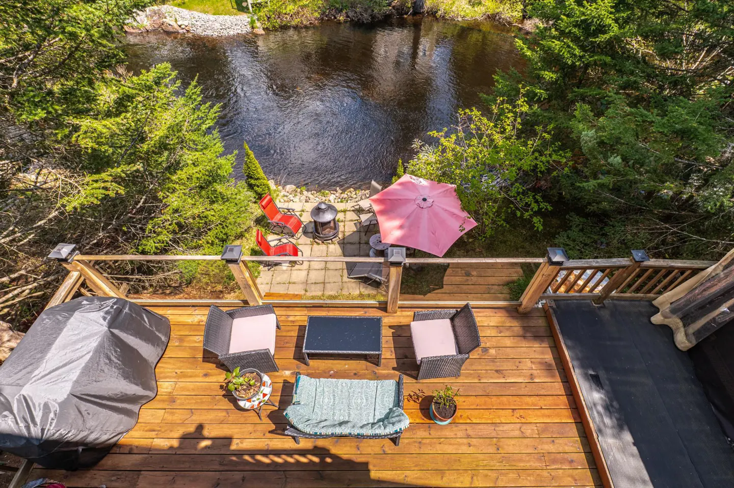 Aerial view of a wooden deck with outdoor furniture overlooking a river surrounded by trees.
