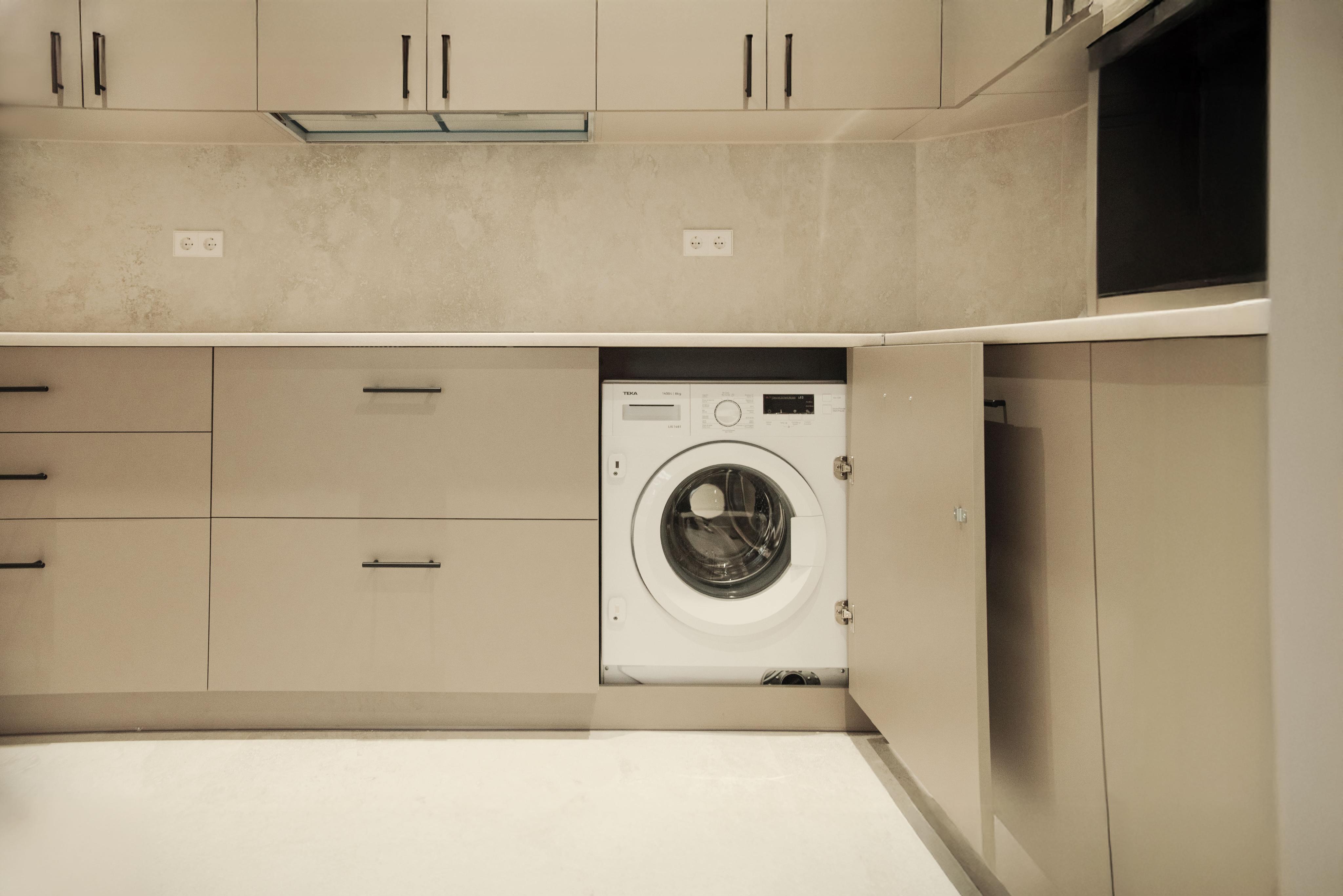 Modern kitchen with beige cabinets and black hardware. A white washing machine is built into the cabinetry.