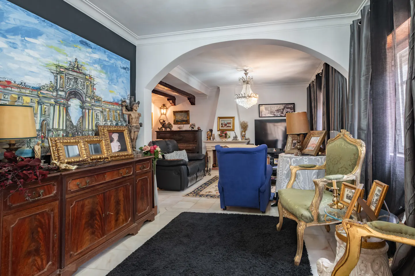 A living room with antique furniture, a large painting, and an archway leading to another room.