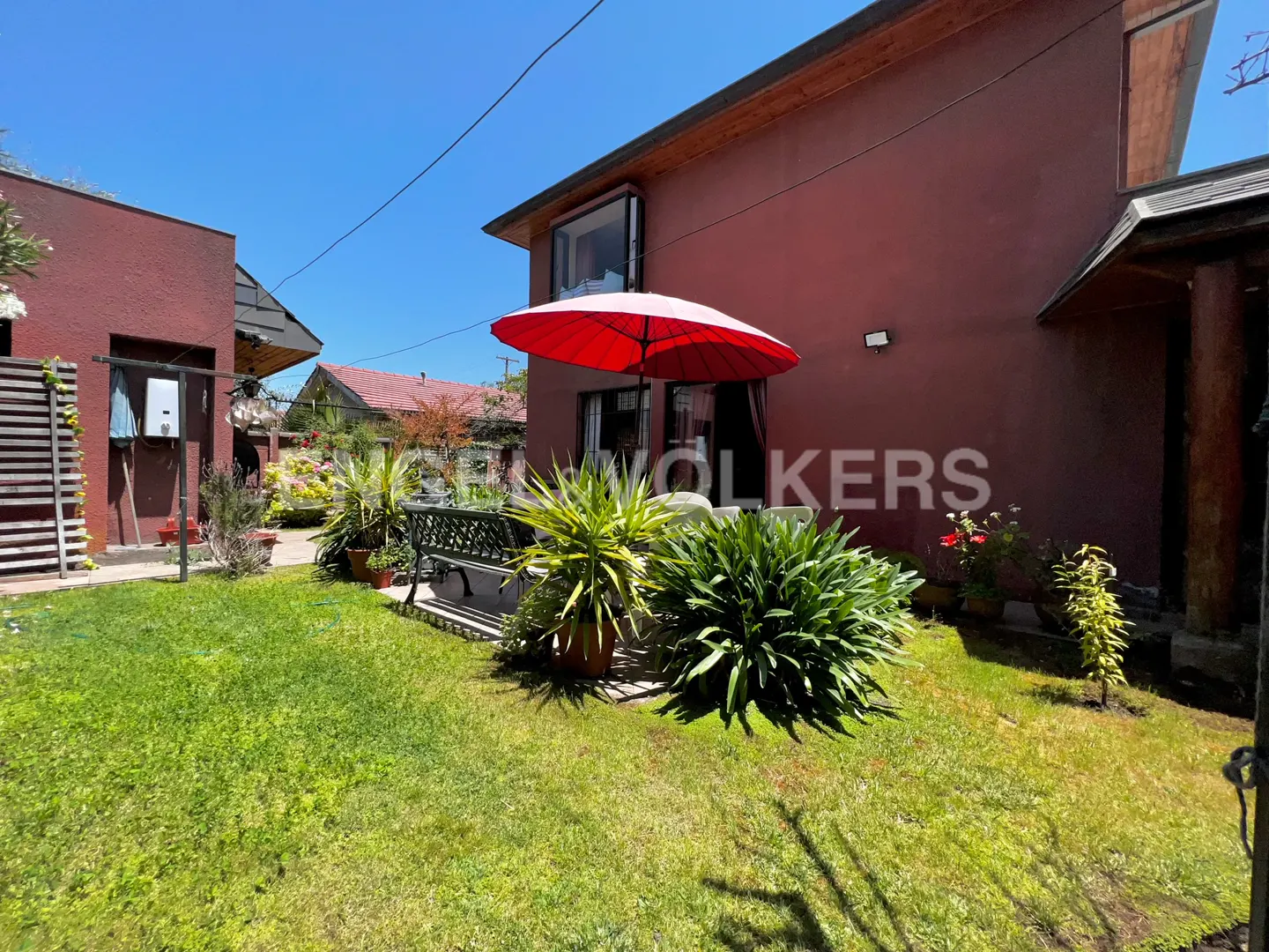 Backyard view of a red house with a red umbrella, green grass, and plants.