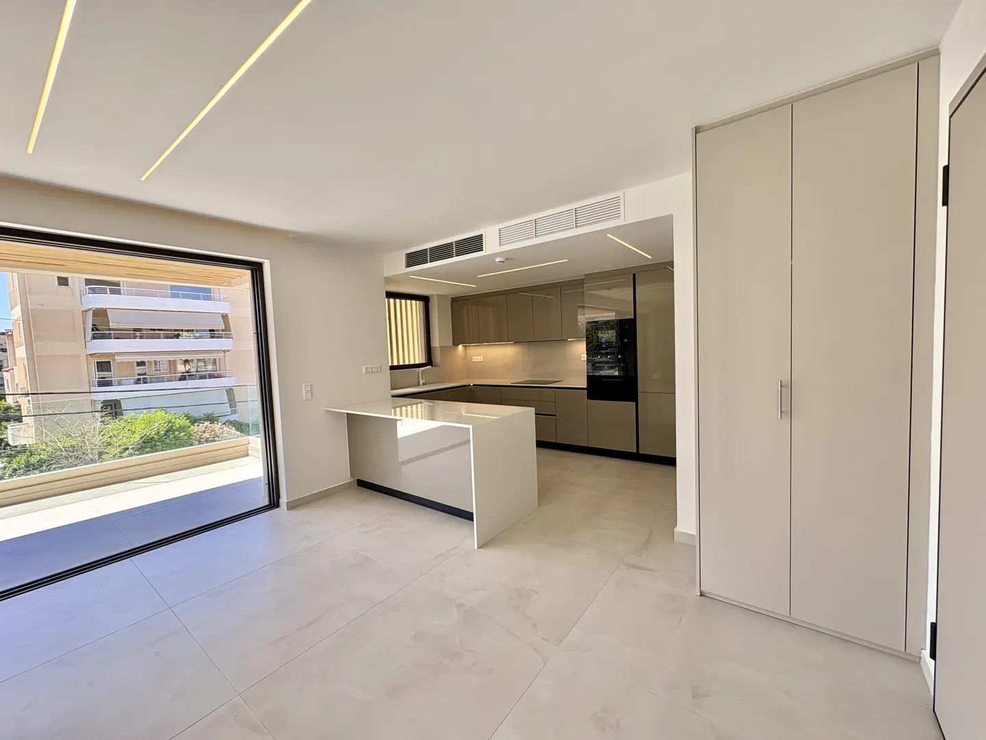 A modern apartment interior with a kitchen, island, and balcony. Neutral tones and sleek design.