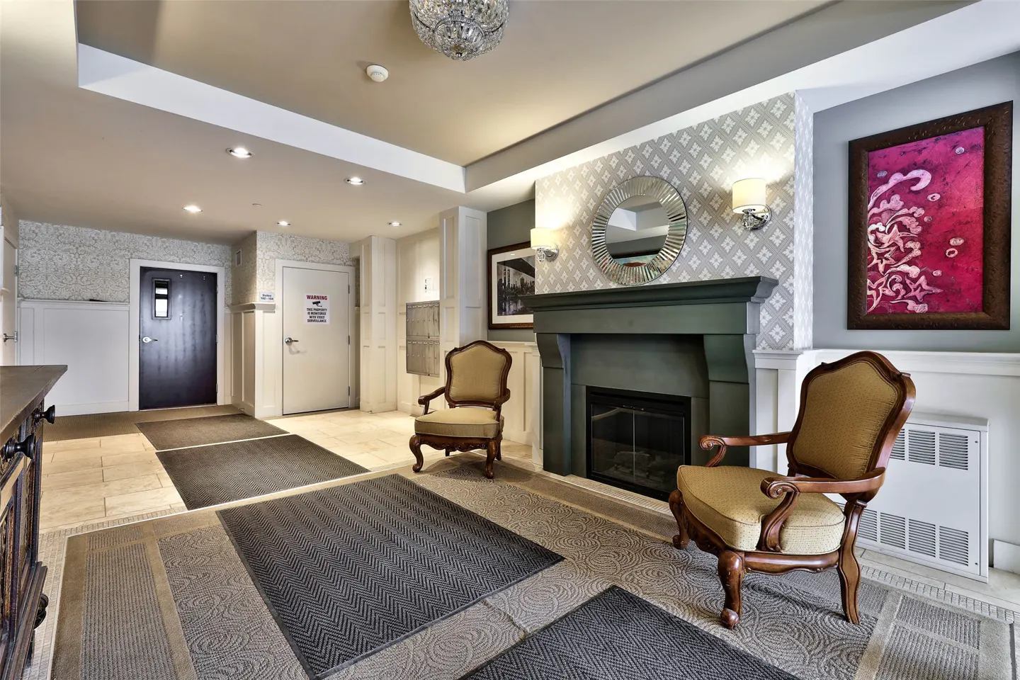 A condo lobby with two chairs facing a dark green fireplace with a round mirror above it.