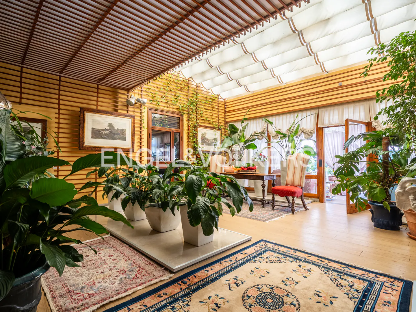 Bright sunroom with wood walls, a slatted ceiling, and a retractable awning. Potted plants and rugs add warmth to the space.