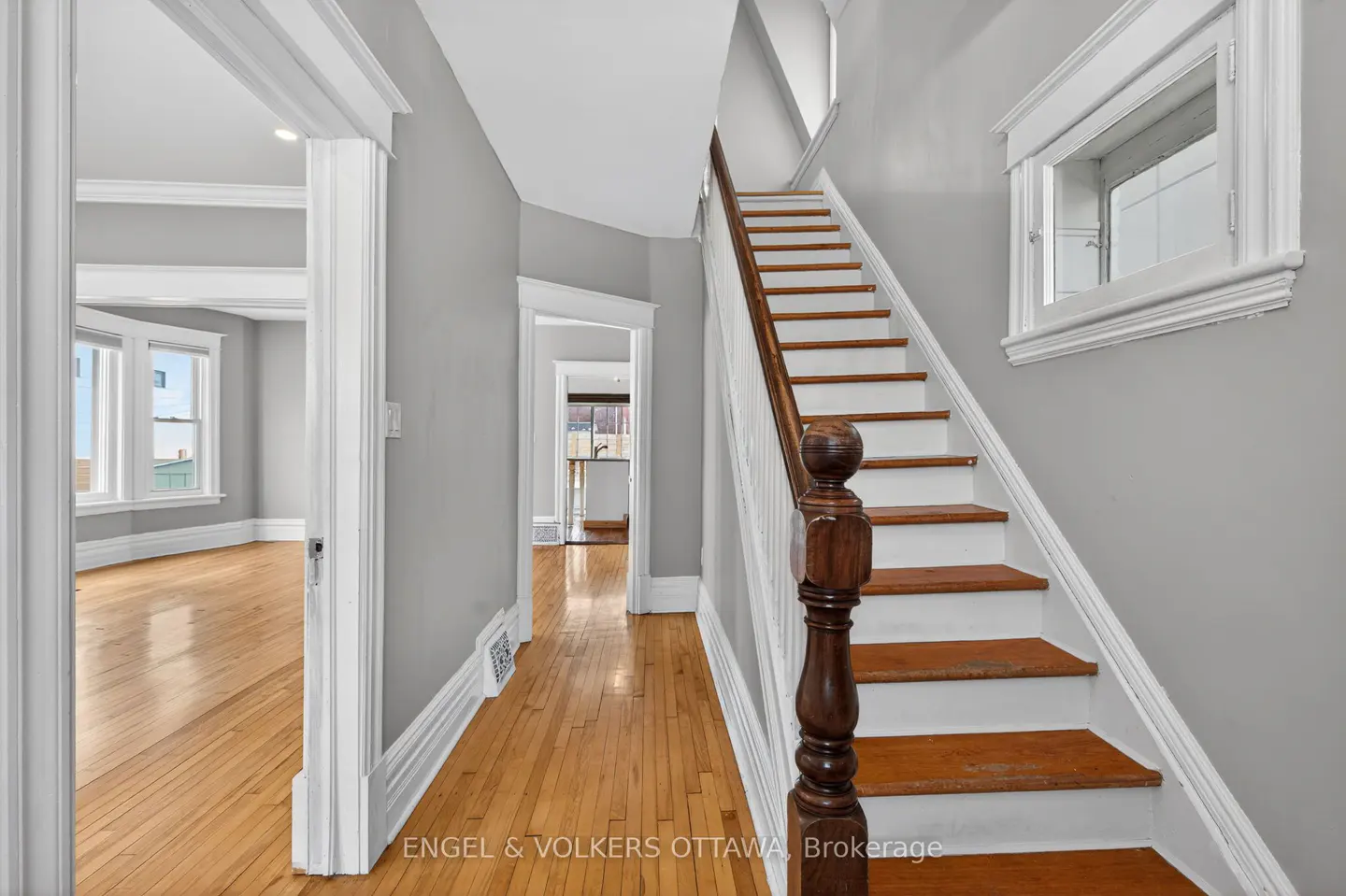 Foyer with hardwood floors, gray walls, and white trim. A staircase with wood treads and white risers leads upstairs. Rooms visible through doorways.
