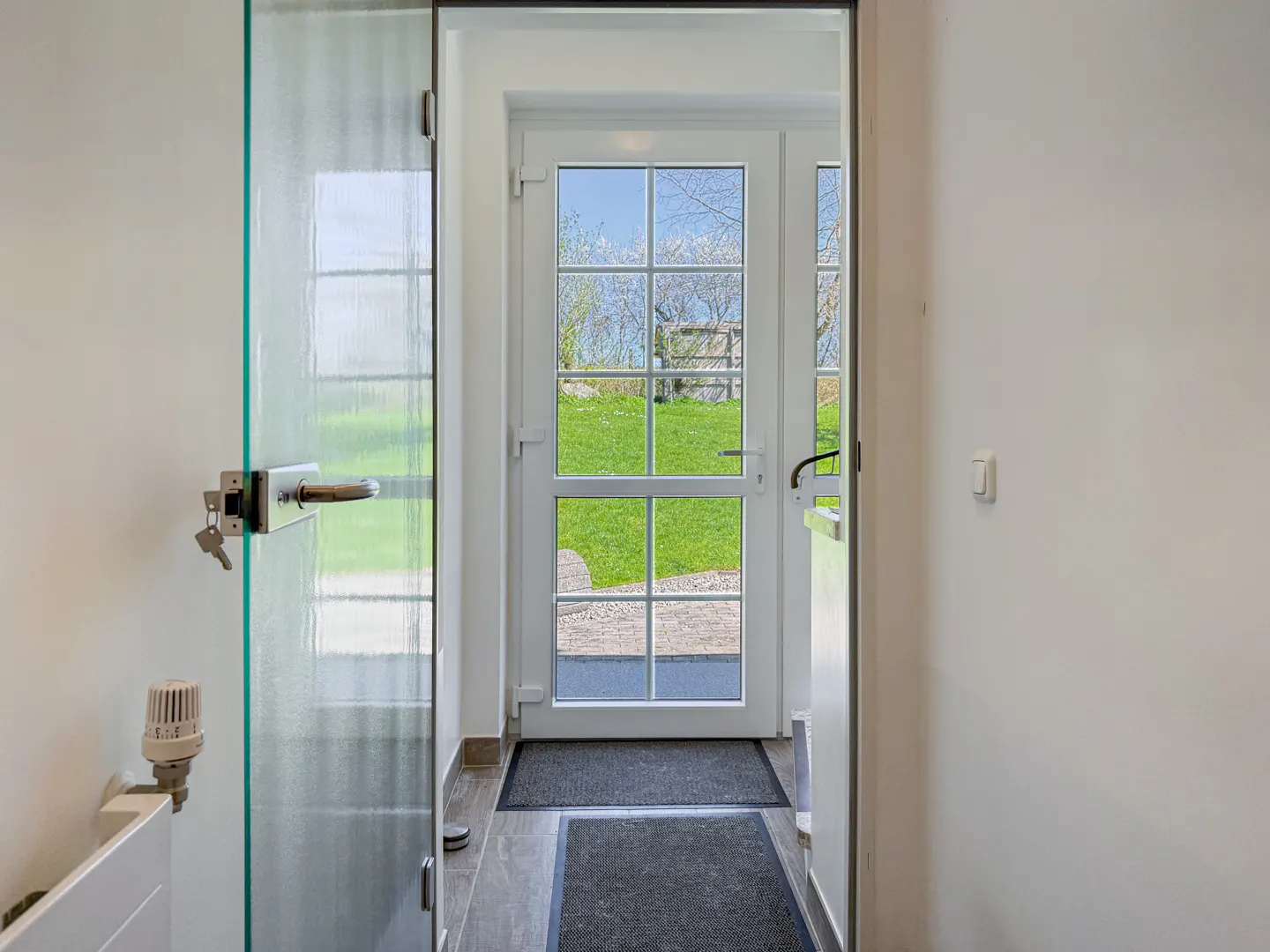 Hallway view with a glass door on the left and a white door straight ahead, leading to a green lawn.