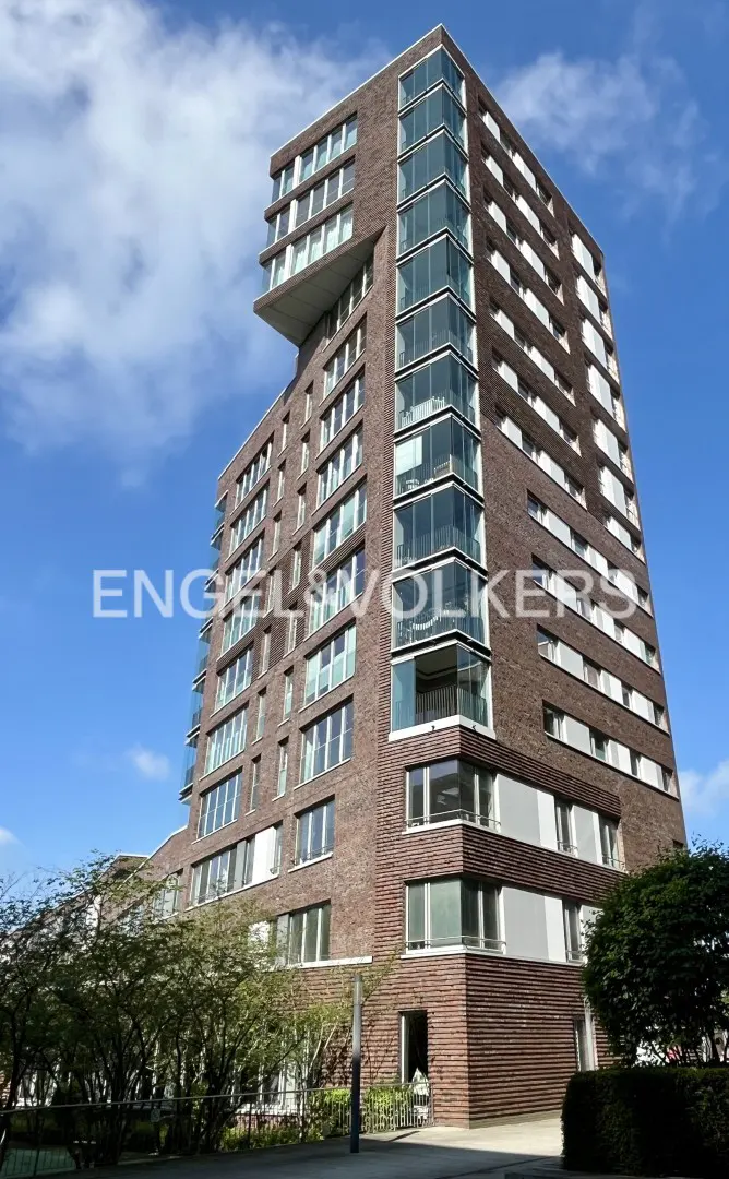 Exterior view of a tall, modern brick apartment building with large windows against a blue sky.