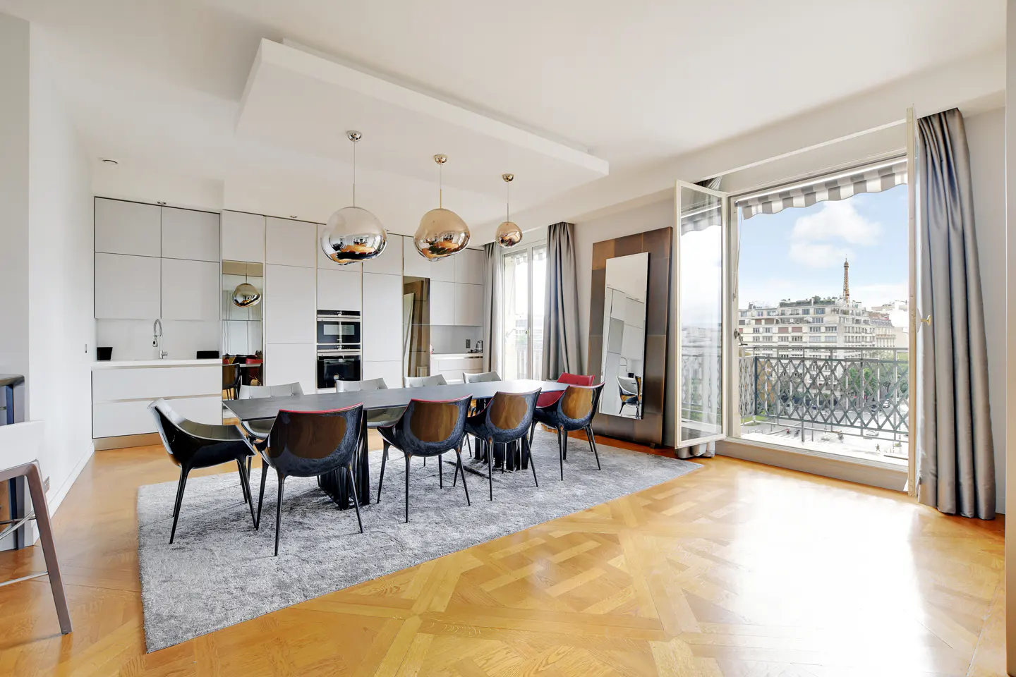 Bright, modern apartment with a dining table, chairs, and a view of the Eiffel Tower through open balcony doors.
