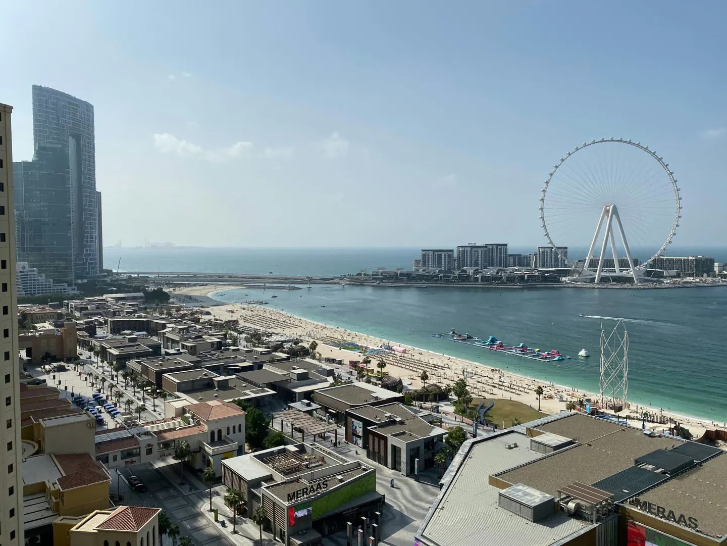 Dubai skyline view featuring Ain Dubai Ferris wheel, beach, buildings, and blue sea under a clear sky.